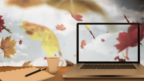 computadora de escritorio y equipos de oficina en una mesa contra las hojas de arce de otoño flotando en el cielo azul