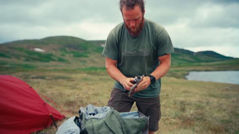 El-Hombre-Está-Empacando-Su-Equipo-De-Campamento-En-La-Orilla-Del-Lago-Interior-Kjøåkertjønna-En-Osen,-Trøndelag,-Noruega---Toma-Estática