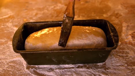 olive oil being brushed over dough in loaf tin on a floury table