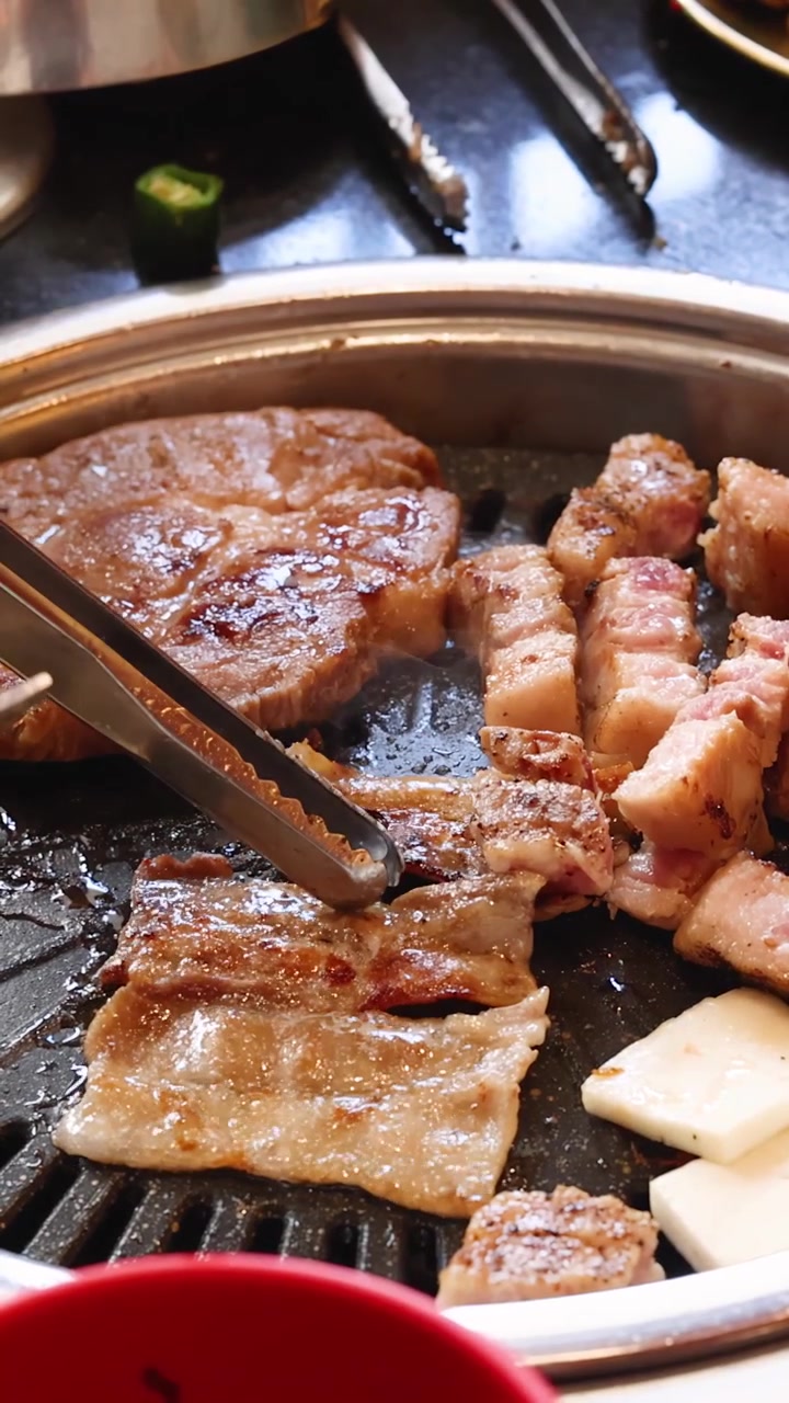 Penjepit membalik perut babi mendesis dan daging marinasi di wajan panggangan barbekyu Korea panas