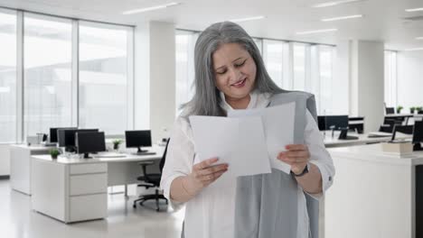 gelukkige indiase senior vrouwelijke manager die zakelijke rapporten leest