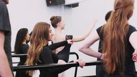 male and female students at performing arts school rehearsing ballet in dance studio using barre