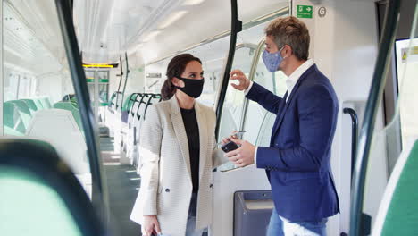 business commuters stand in train carriage with mobile phones wearing ppe face masks during pandemic