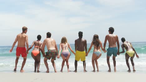 Front-view-of-mixed-race-friends-jumping-together-on-the-beach-4k