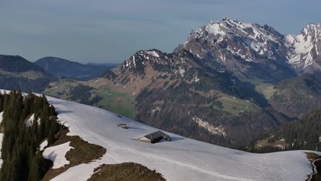 Aerial-view-of-houses-nearly-half-buried-in-snow-at-the-Amden-ski-resort,-with-the-giant-and-imposing-Säntis-mountain-in-the-background