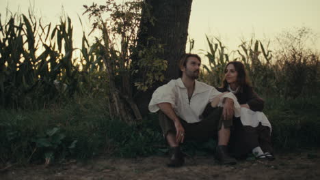 couple in period costumes relaxing in a rural field at dusk