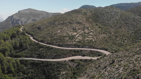 aerial wide shot red car drives through paved road mountain turns tracking shot