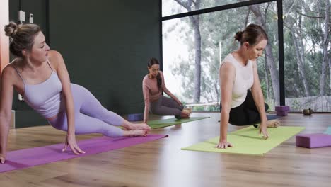 mujeres diversas estirándose juntas en esteras en la clase de yoga con una entrenadora femenina, cámara lenta