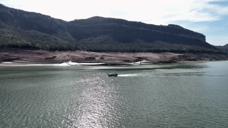 Local-boat-sailing-on-drying-lake-in-Spain-during-drought-season,-aerial-view