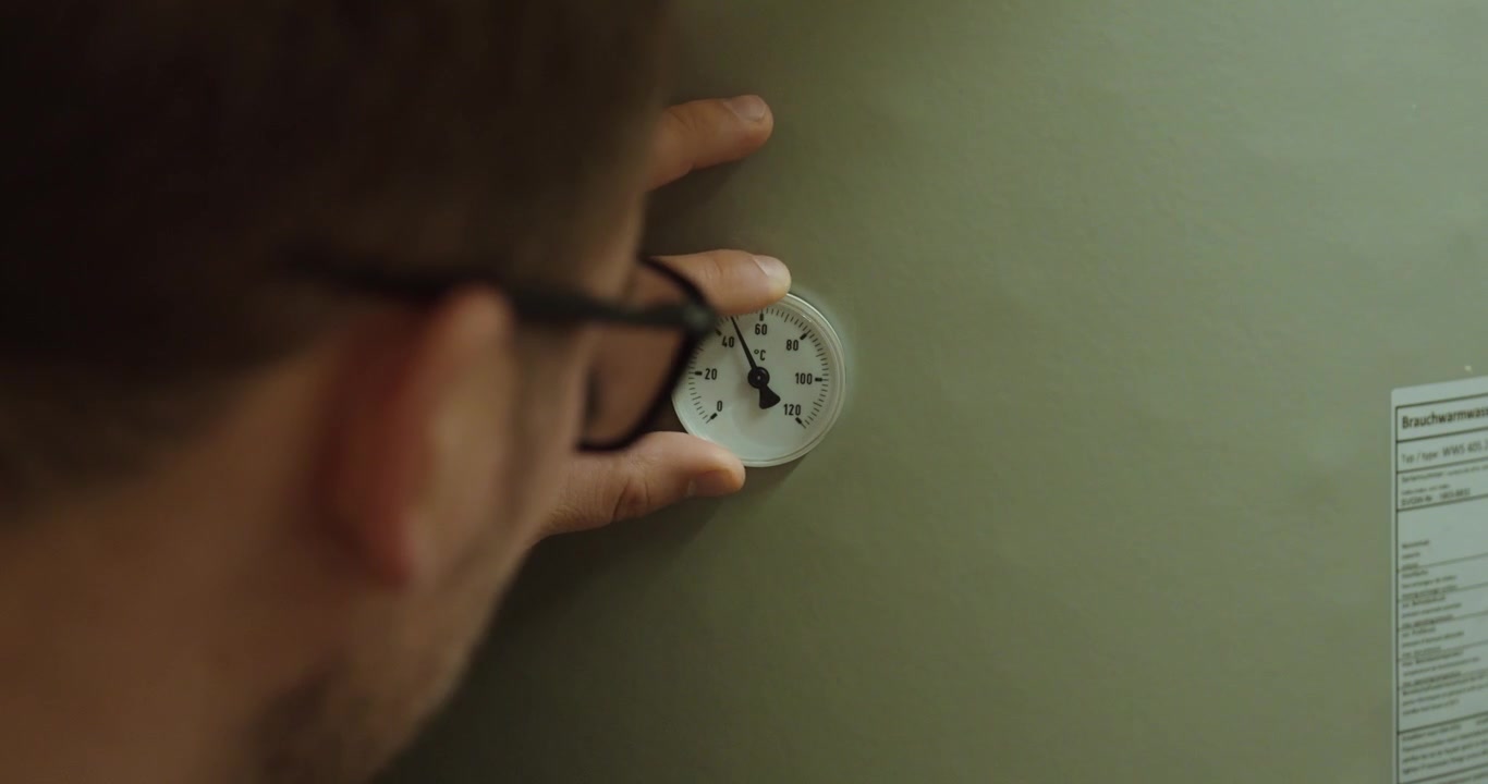 man inspecting and checking a thermostat or temperature gauge on a heating system. Concept of HVAC maintenance, energy efficiency, heating control, technical inspection, home utilities, and building m