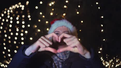 woman celebrates christmas, smiling and showing shape of heart with her hands