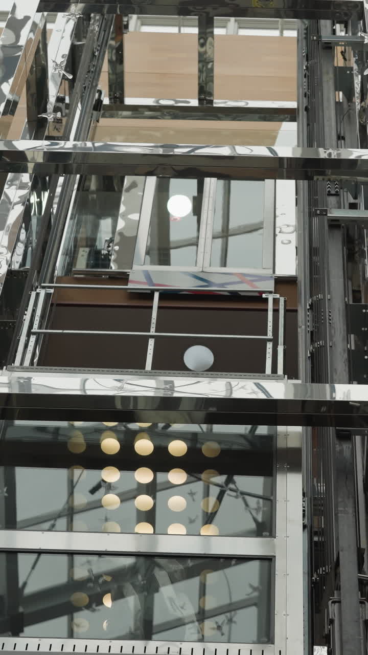 Modern glass elevators in motion, one ascending and one descending, surrounded by reflective metallic structure and architectural details
