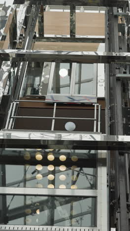 elevadores de vidrio modernos en movimiento, uno ascendente y otro descendente, rodeados de estructura metálica reflectante y detalles arquitectónicos