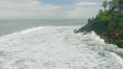 4K-Luftbildaufnahme-Des-Klippenstrandes-Von-Varkala-Mit-Vielen-Cafés,-Sich-Bewegenden-Wolken-Im-Hintergrund-Und-Wellen,-Die-Morgens-Am-Fuß-Der-Klippe-Brechen