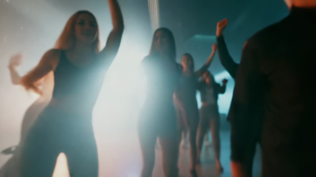 Fog haze and orange blue lights sparking dancers in athletic wear stepping, raising arms in studio