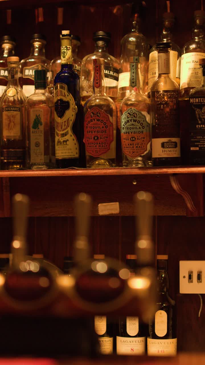 Ripresa con tilt verticale lento di varie bottiglie di whisky scozzese su scaffali di legno in penombra