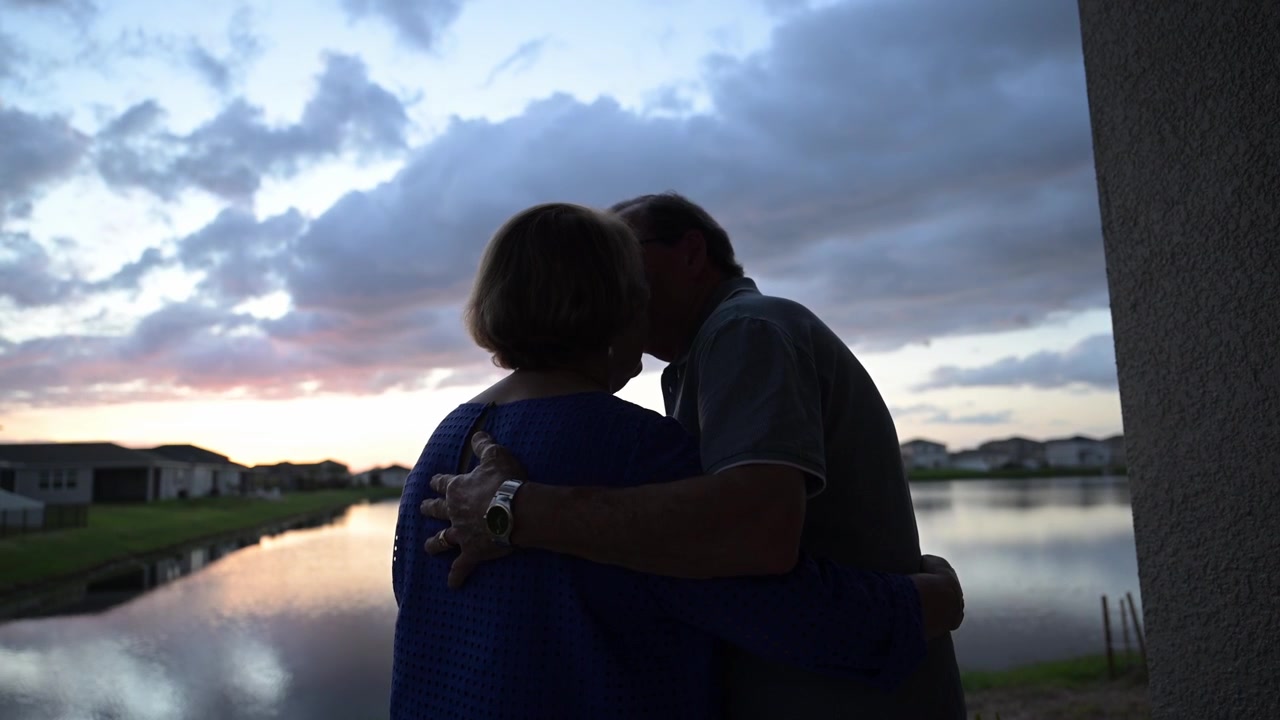 loving senior citizen couple embrace lookup up in the sky during sunset after a tumultuous hurricane near their home