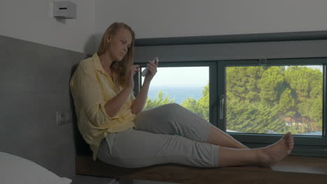 woman sitting on window-sill and using phone