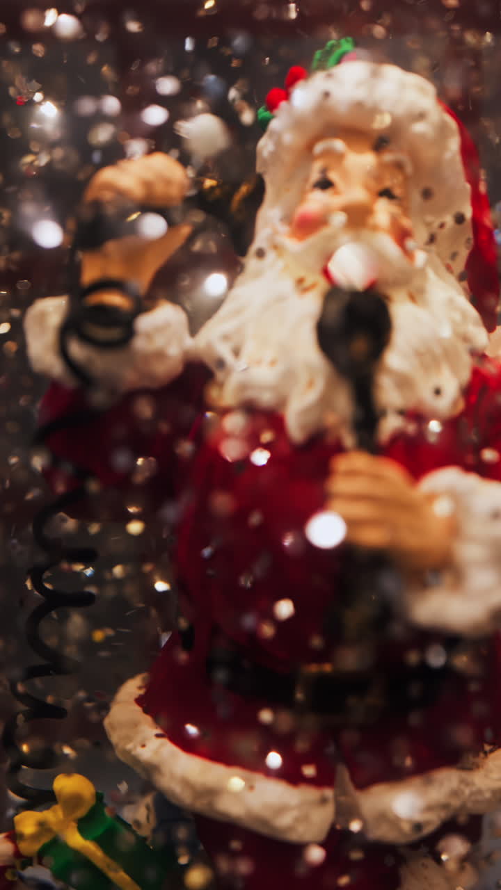 Close up of a Santa Clause figurine in a snow globe with sparkles floating in it. Vertical