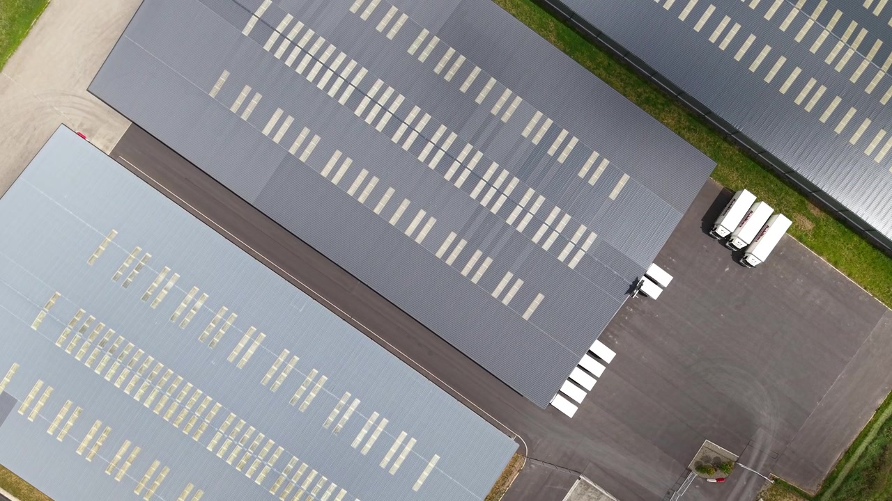 Et luftfoto viser et industrielt lageranlæg og dets parkeringsplads, der fremviser moderne logistikinfrastruktur og organisering af kommercielle områder.