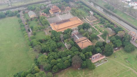 Drone-aerial-view-in-Vietnam-flying-over-Hue-imperial-stone-brick-fortress-wall,-green-gardens,-temples-and-canals-on-a-cloudy-and-foggy-day