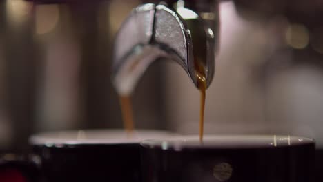 a metallic double spout is seen up close as espresso flows from it into two separate glass espresso cups