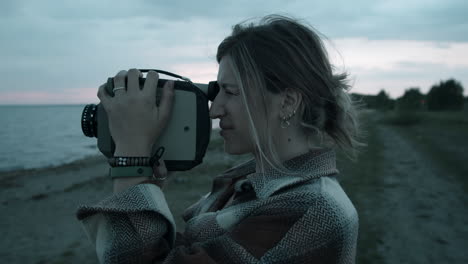 mujer usando una cámara de cine retro en la orilla del lago por la noche