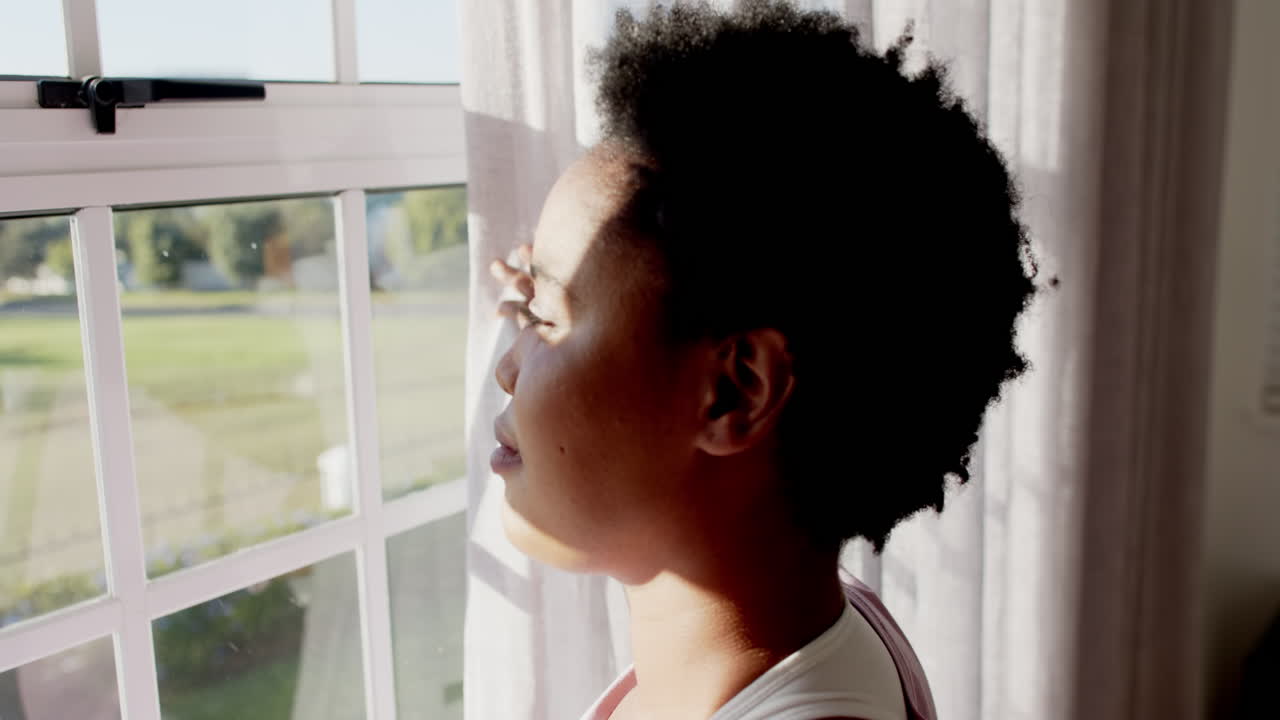 African American woman enjoys sunlight by the window at home