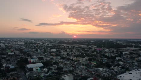 Vista-Aérea-De-Un-Pueblo-Y-Detrás-Hay-Una-Hermosa-Puesta-De-Sol-Que-Pinta-El-Cielo-Con-Tonos-Cálidos-Y-Brillantes,-Playa-Del-Carmen