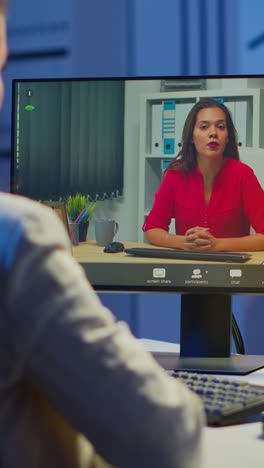 vertical video: manager talking with coworker during video conference at midnight