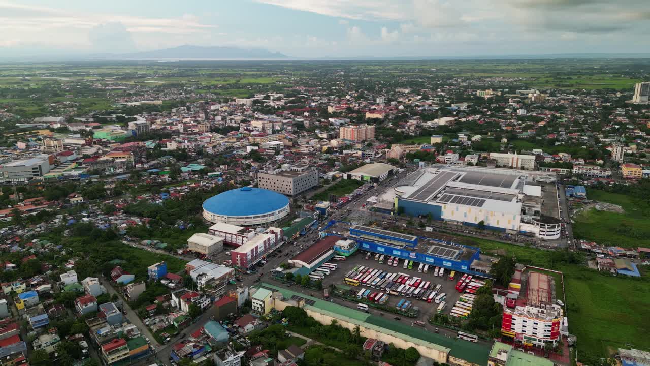 Panoramic aerial orbit of bus terminal along busy roads, Jesse M Robredo Coliseum, and buildings in Naga City business district, Philippines