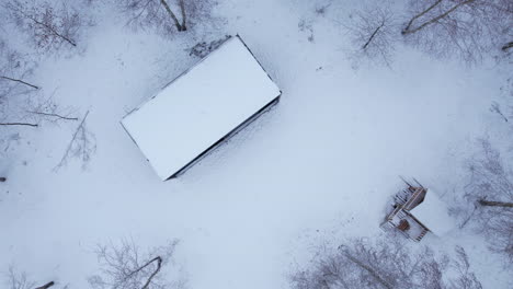 aerial birds eye flying over remote snow covered rooftop in winter forest