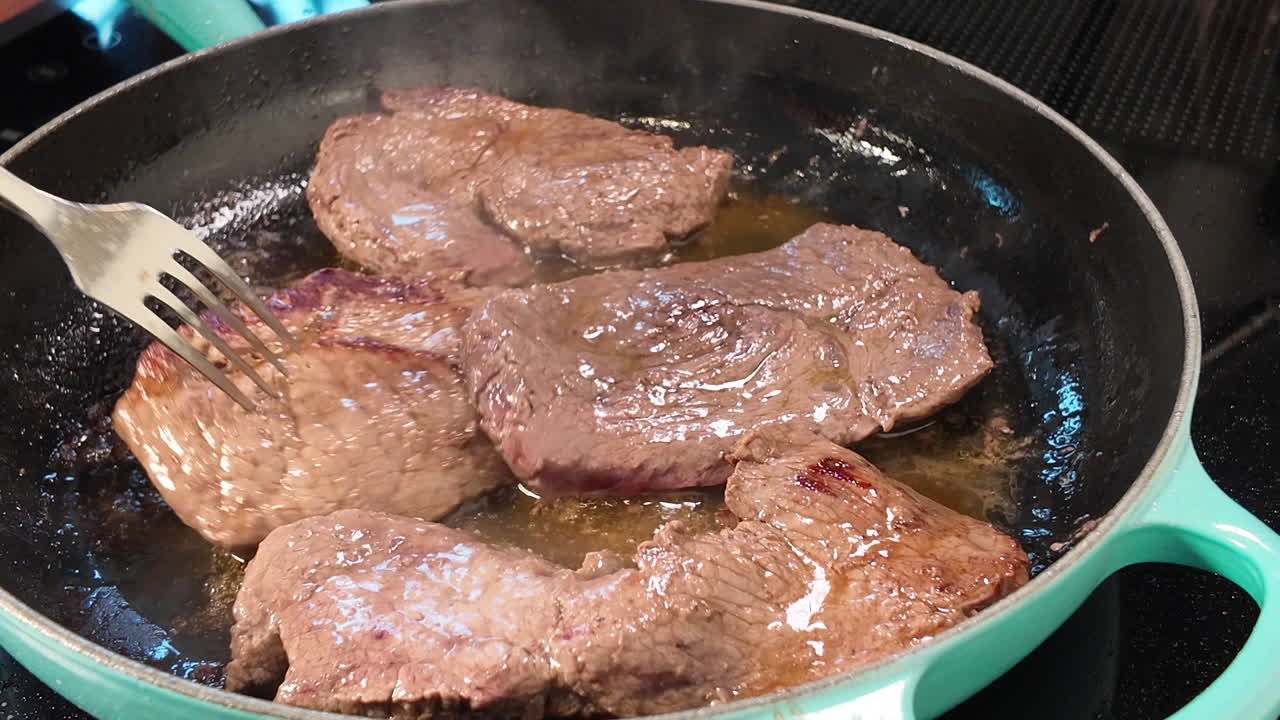 Pengambilan gambar close-up dari steak daging sapi yang dibalik dalam wajan penggorengan panas dengan minyak di atas kompor modern