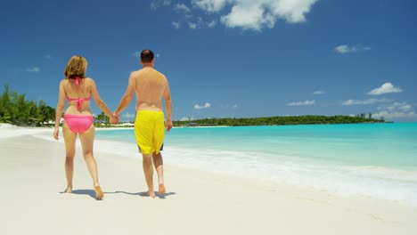 young caucasian couple walking on white sand beach