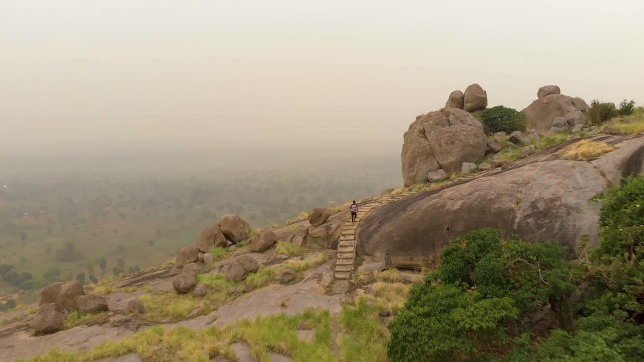 toma aérea siguiendo a un hombre africano corriendo por una escalera en una montaña de granito en áfrica