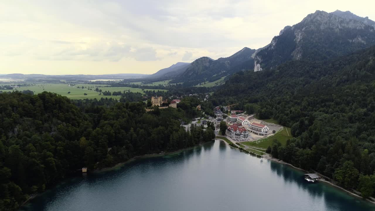 Flying over lake Alpsee towards castle Hohenschwangau having castle Neuschwanstein and the alps mountain landscape scenery in the background