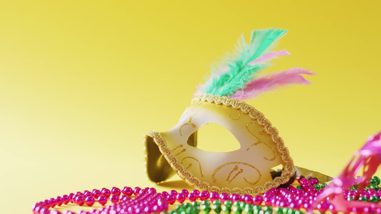 Video of masquerade mask with feathers and mardi gras beads on yellow background with copy space