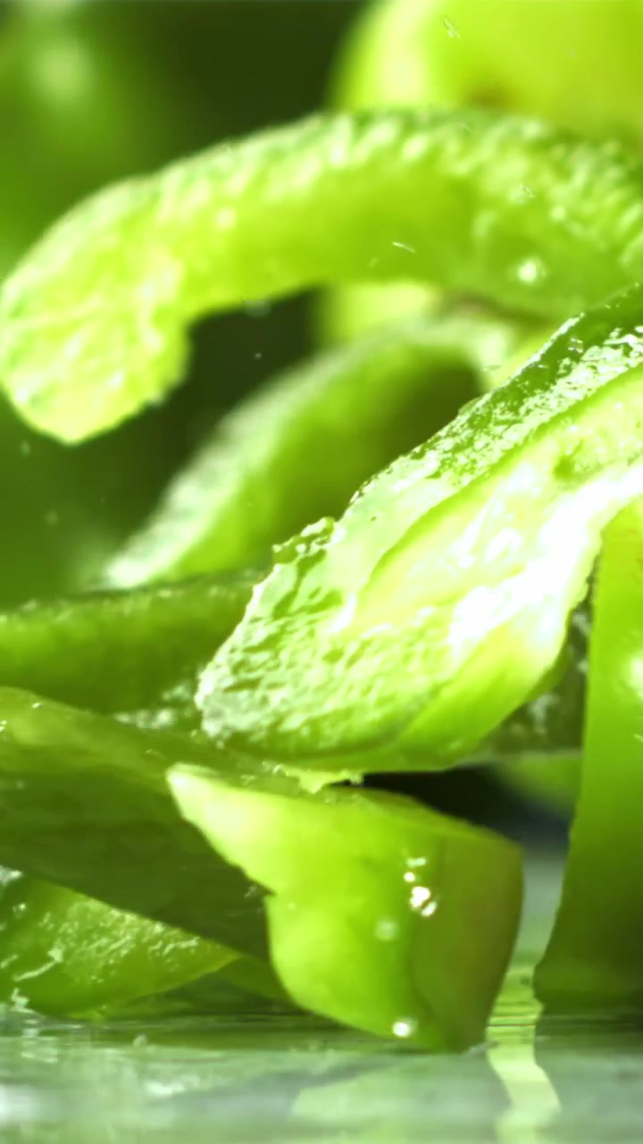 Fette fresche di peperone verde che cadono al rallentatore.