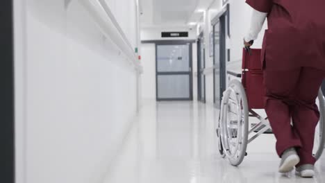 african american female doctor running with wheelchair in hospital corridor, slow motion