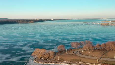Aerial-shot-of-massive-frozen-lake-with-park-with-walking-trails