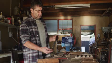 Caucasian-male-knife-maker-in-workshop,-holding-and-checking-knife