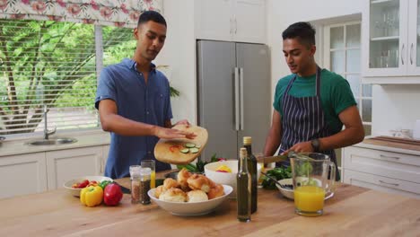 Happy-mixed-race-gay-male-couple-talking-and-preparing-food-in-kitchen