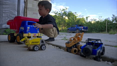 slow motion panning of a young mexican latin boy playing with his toy trucks on his house driveway in the afternoon