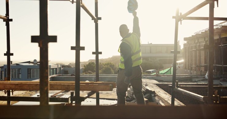 Construction Worker Celebrating Success on Building Site at Sunset