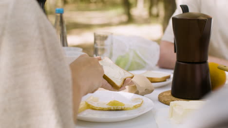 Nahaufnahme-Einer-Nicht-Erkennbaren-Frau,-Die-Butter-Auf-Toast-Verteilt,-Während-Sie-Im-Freien-Frühstückt