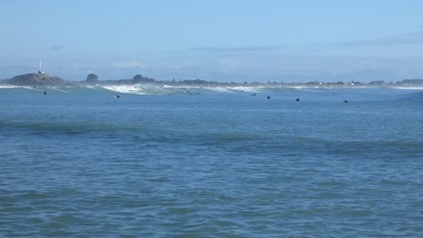 Small-waves-roll-gently-into-shore-on-a-sunny-day-as-surfers-try-to-catch-a-ride---Scarborough-Bay,-New-Zealand