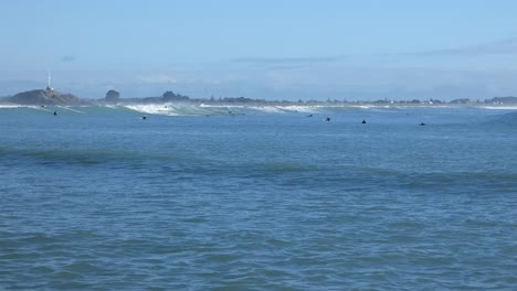 small waves roll gently into shore on a sunny day as surfers try to catch a ride - scarborough bay, new zealand