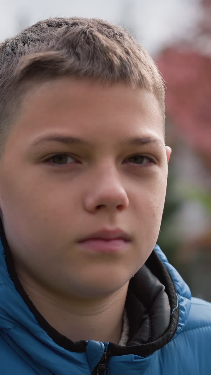 primer plano de un niño con una chaqueta azul al aire libre, mirando pensativo, con árboles de otoño borrosos y una casa con techo rojo borrosa en el fondo