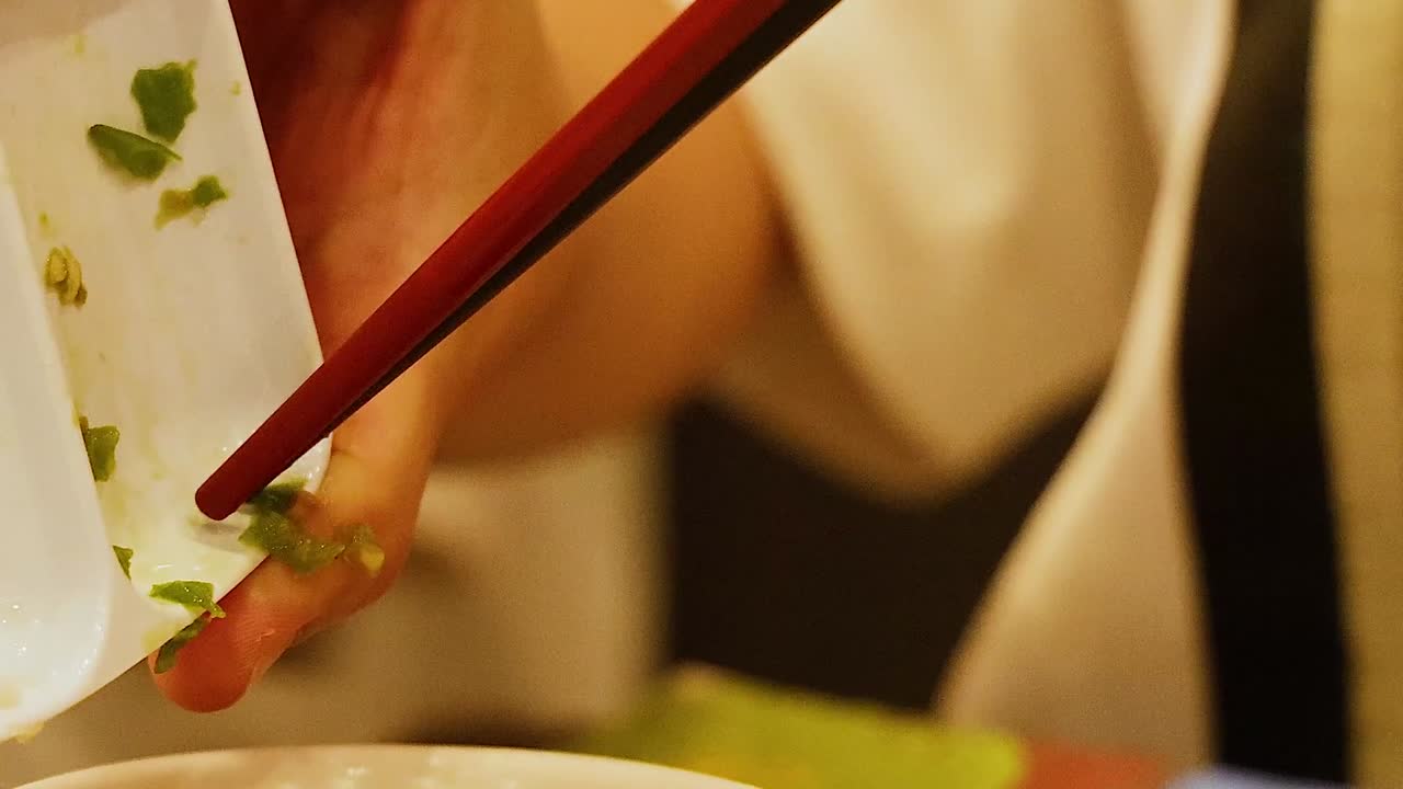Close-up of hands using chopsticks to transfer herbs into a bowl, focusing on precise culinary technique.