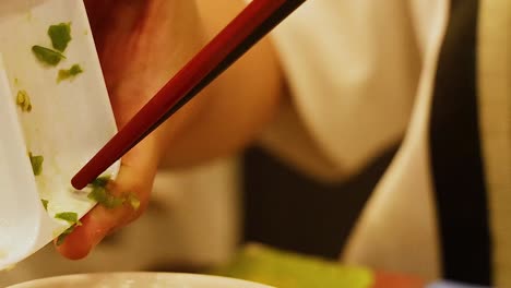 close-up of hands using chopsticks to transfer herbs into a bowl, focusing on precise culinary technique.